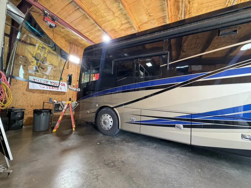 Large motorhome windshield held by lifting equipment next to a coach